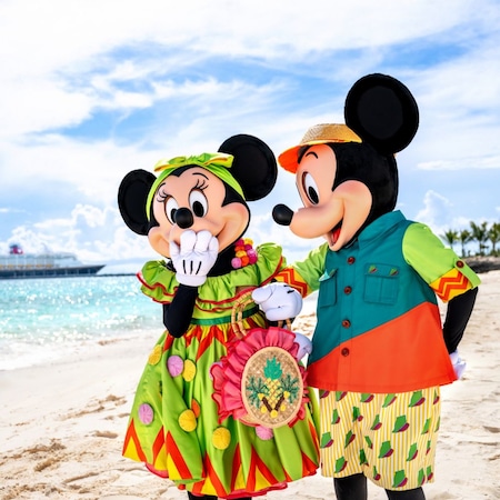 Mickey Mouse and Minnie Mouse in Junkanoo outfits standing on a Bahamian beach with a Disney Cruise Line ship on the horizon