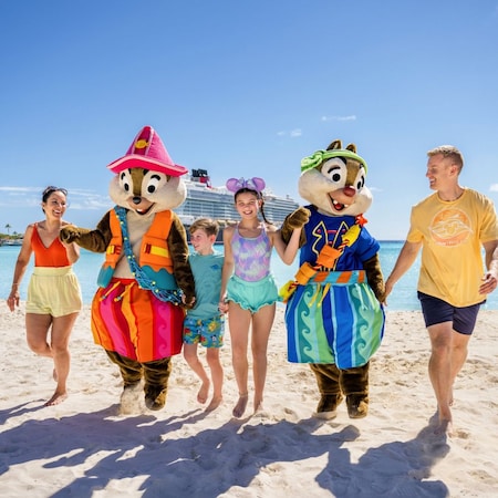 Chip and Dale holding hands with a family of 4 while walking on the beach