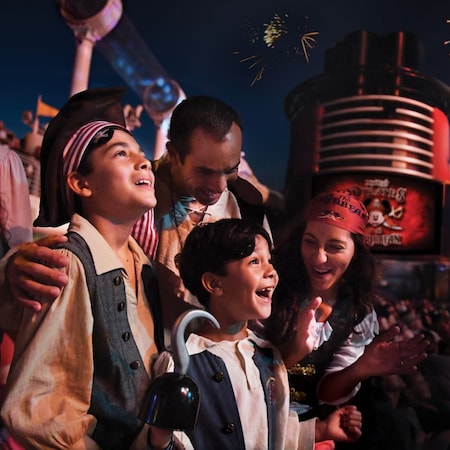 A family of 4 dressed in pirate attire watching a fireworks display during a deck party at sea