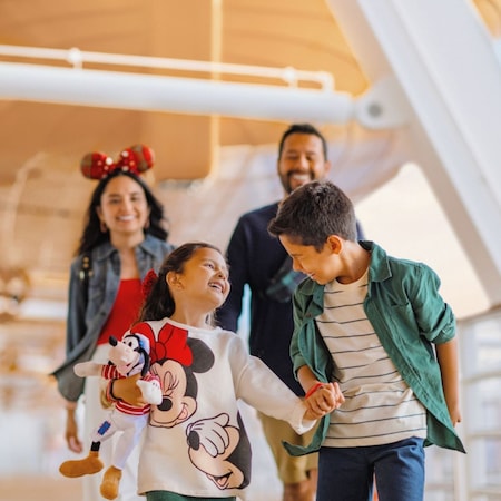 Família sorridente vestindo trajes temáticos da Disney caminhando junta no deck de um navio da Disney Cruise Line