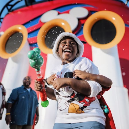 A young Guest holds a Mickey shaped bubble wand near a Disney Cruise Line ship’s funnel