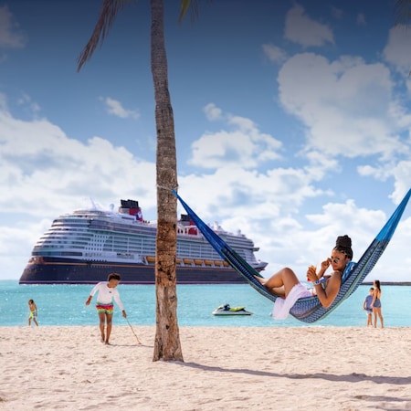 A woman relaxing in a hammock between palm trees on a beach with a Disney Cruise Line ship in the distance