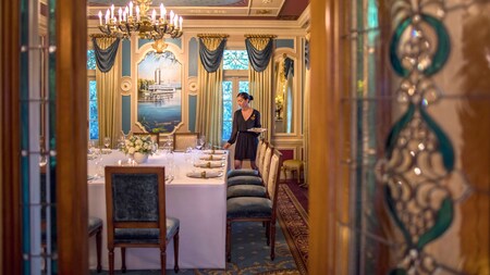 A Cast Member sets a table in a private dining room at 21 Royal in Disneyland Park