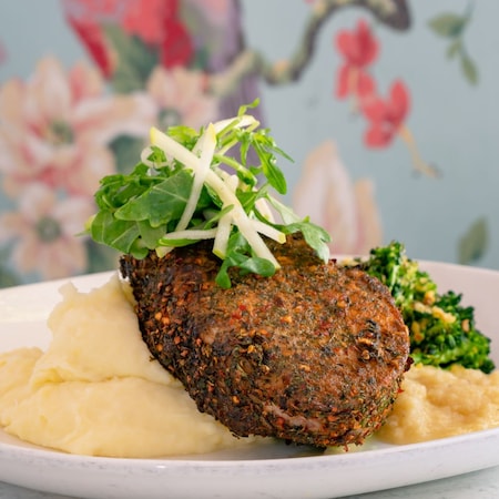 Chuleta de cerdo servida con puré de papas y verduras de hoja.