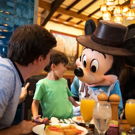Mickey Mouse visita a un niño y a su padre mientras comen en una mesa