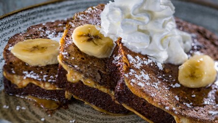 Three slices of Banana Bread French Toast topped with powdered sugar and whipped cream