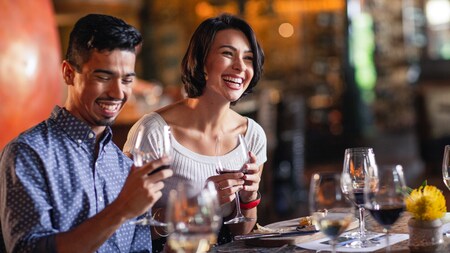 A man and a woman laugh while drinking wine in a restaurant