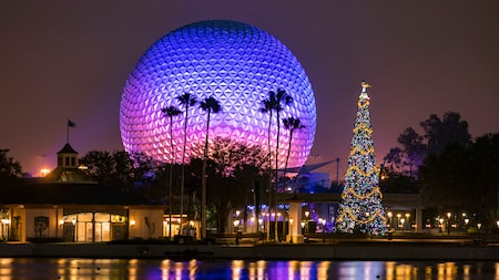 A Christmas tree in front of a cluster of palm trees and the Spaceship Earth attraction