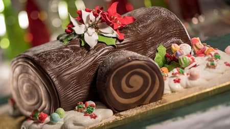 A yule log decorated with festive flowers and small figurines of gingerbread men and candy canes