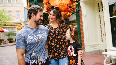 A young family of 3 wearing Disney Halloween apparel smile at each other while at Walt Disneyland World Resort