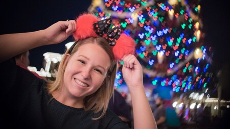 A woman wearing Minnie Mouse ears in front of a Christmas tree