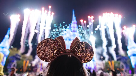 A girl wearing Minnie Mouse ears watching fireworks burst around Cinderella Castle