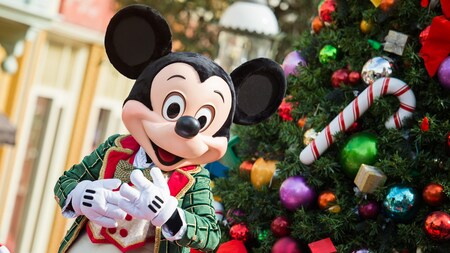 Mickey Mouse standing next to a Christmas tree