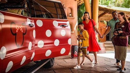 Una familia se sube a bordo de un vehículo del servicio Minnie Van en un hotel de Disney mientras un Miembro del Elenco observa