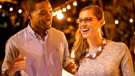 A man and woman smile together at night with many lights shining in the background