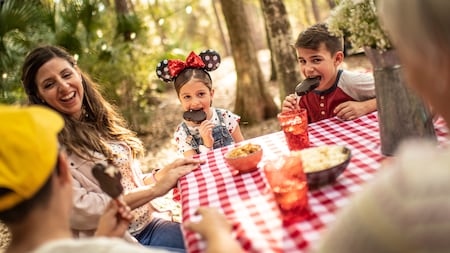 Une mère riant alors que ses 3 enfants mangent des barres de crème glacée Mickey Mouse à une table de pique-nique