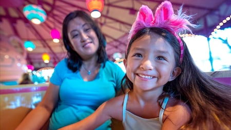 A girl wearing a fuzzy headband rides the Mad Tea Party with her mother