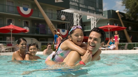 Family of 4 laugh while playing in the pool at Disney’s All Star Sports Resort