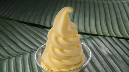 A pineapple soft serve dessert in a clear bowl on banana leaves