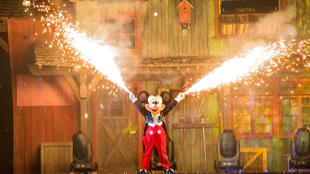 On a performance stage, Mickey Mouse shoots fire out of his fingertips