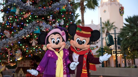 Mickey Mouse and Minnie Mouse in holiday attire, posing in front of a Christmas tree