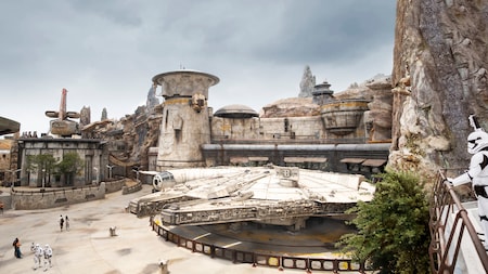 A First Order stormtrooper looks on at the Millennium Falcon docked below exotic Star Wars buildings and petrified wood spires
