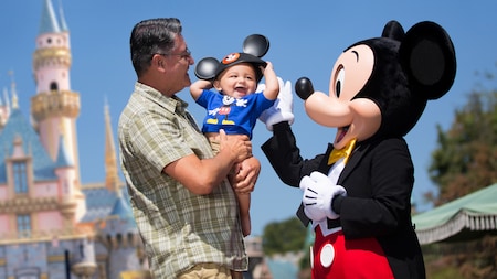 A man holds a smiling baby near Mickey Mouse and Sleeping Beauty Castle