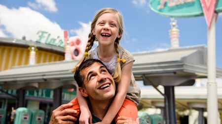 A smiling girl rides on a man's shoulders near Flos V8 Cafe