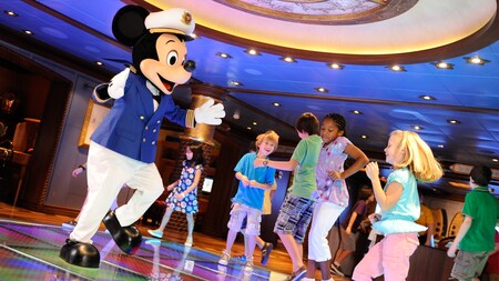 Mickey Mouse dances with kids in the central rotunda of Disneys Oceaneer Club on a Disney cruise ship