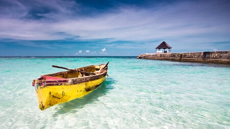 An old rowboat floats in clear waters next to a breaker with a small gazebo structure