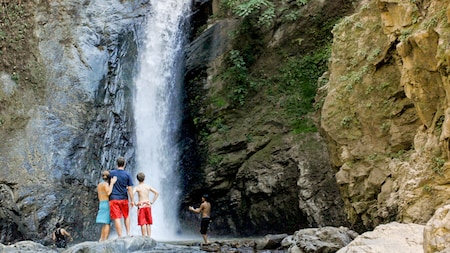 People stand in front of a tall waterfall pouring down a rock face