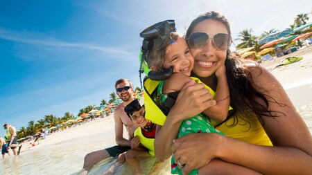 A young mother at the beach hugs her small daughter while her husband and son watch