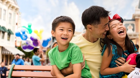 Un padre abraza a sus 2 pequeños niños alegremente en Main Street U.S.A.