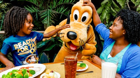 A girl and her mother sitting at a lunch table scratch Pluto's head