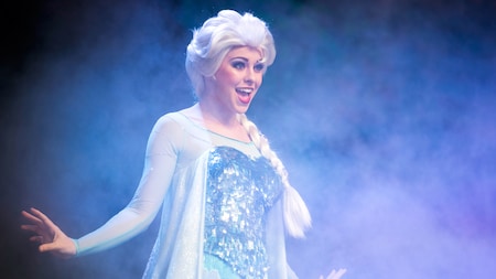 Queen Elsa sings on stage, surrounded by an icy mist