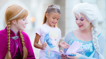 A little girl with a tiara and an Elsa shirt gets autographs from the real Anna and Elsa