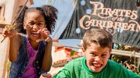 A young girl and boy growl and strike intimidating pirate poses in front of the Pirates of the Caribbean attraction