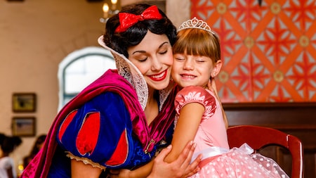 Snow White abraza a una niña con un vestido de princesa y una corona sentada a su lado
