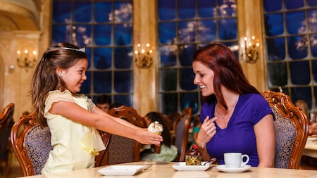 Una joven Huésped con una tiara sostiene un cupcake durante una experiencia culinaria en el restaurante Be Our Guest