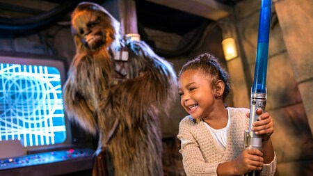 An excited young girl plays with a toy lightsaber at a Character Greeting experience with Chewbacca