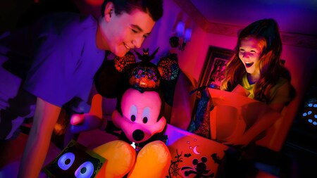 A brother and sister delight in an illuminated Halloween themed plush Mickey inside their Disney Resort hotel room