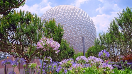 Spaceship Earth ascends into the sky while surrounded by flowers and lush greenery at Epcot