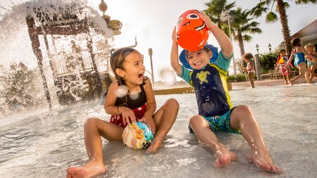 A young girl and her even younger brother splash about in a water play area at a Disney Resort hotel
