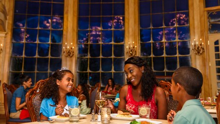 A mother and daughter and son enjoy dinner at Be Our Guest Restaurant in Fantasyland