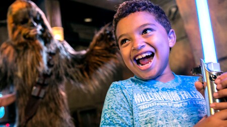 A boy holding a lightsaber, standing near a giant Chewbacca figure