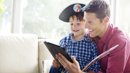 A man and a boy wearing a pirate hat look at a tablet together