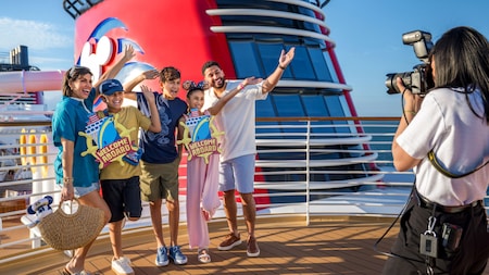 Una familia de cinco personas sostiene letreros que dicen bienvenidos a bordo mientras posan para una foto tomada por un fotógrafo de Disney PhotoPass