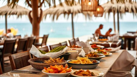 A dining table with a variety of dishes and appetizers on a shaded beachside patio