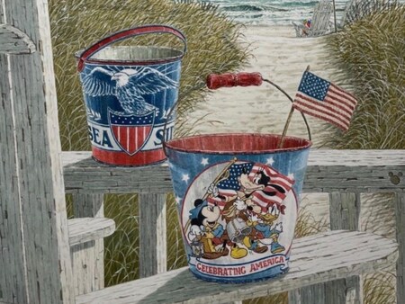 A Disney character bucket with Celebrating America text and an eagle themed bucket on a deck railing overlooking a beach path to the ocean
