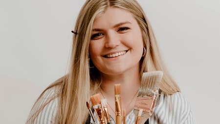 Disney artist Allison Rook smiling and holding paint brushes
